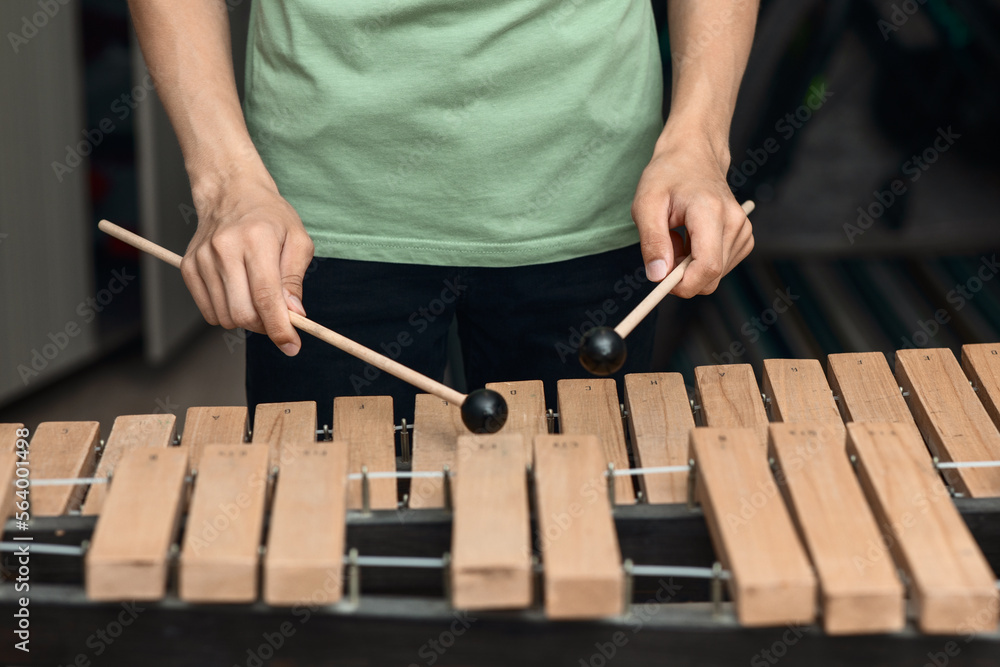 Hands of a young musician playing sticks on a wooden musical instrument xylophone, close-up, selective focus