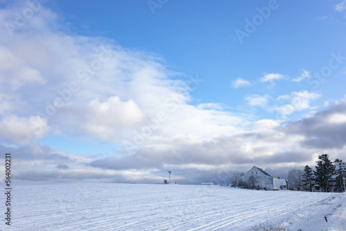 White barn in a snowy northern Maine landscape with a windmill and a variety of clouds from an incoming weather system.