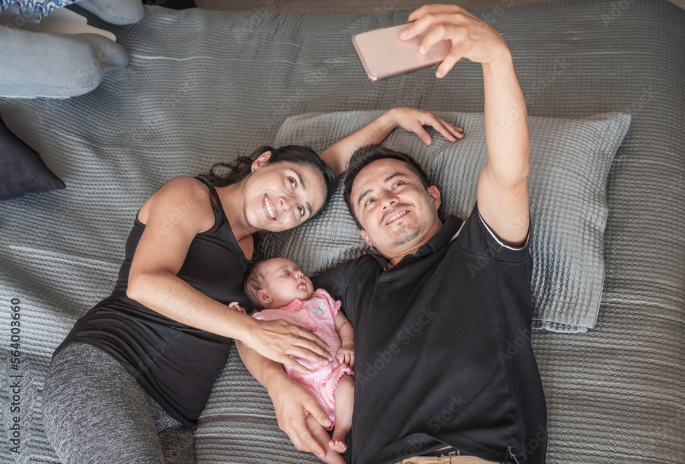 smiling father and mother taking a selfie with their baby in bed