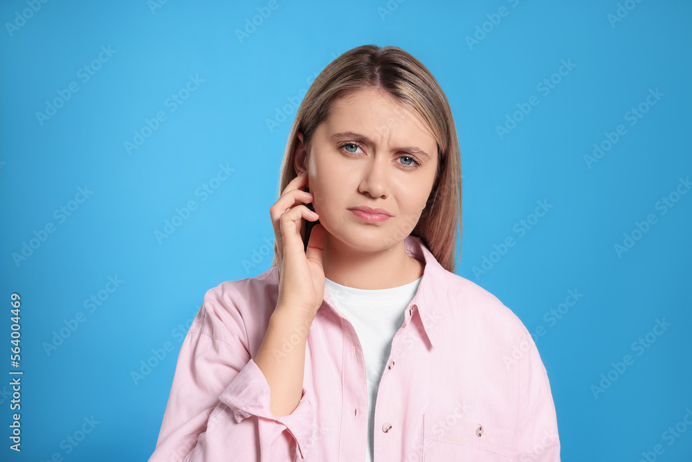 Young woman suffering from ear pain on light blue background Young woman suffering from ear pain on light blue background