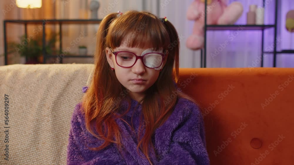 Sick ill preteen girl looking at camera, having protective bandage plaster patch scratch on one eye. Injury, trauma, blind. Child kid wearing glasses at home in room. Medical eyesight vision therapy