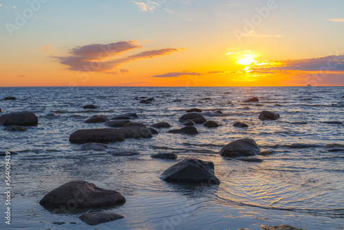 A beautiful scene of sunset sky reflecting on water with boulders of Baltic sea shore