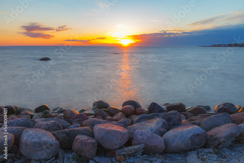 A beautiful scene of sunset sky reflecting on water with boulders of Baltic sea shore © yegorov_nick