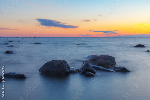 A beautiful scene of sunset sky reflecting on water with boulders of Baltic sea shore