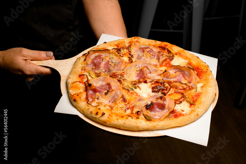 round pizza with bacon on wooden chopping board in male hands