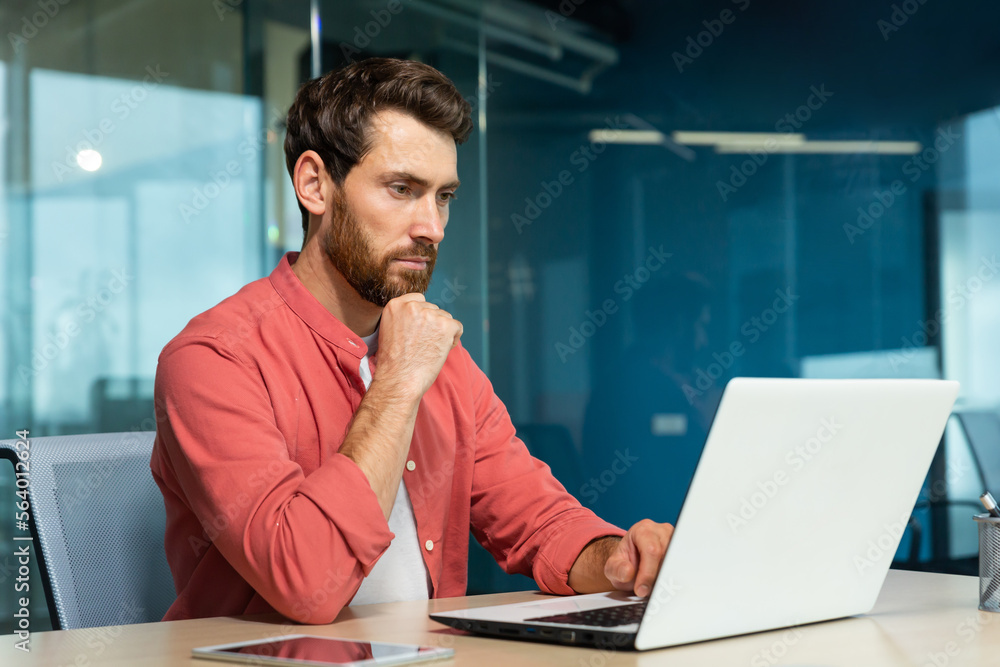 Serious thinking businessman close up, man in red casual shirt working inside modern office, mature boss working with laptop at workplace while sitting Serious thinking businessman close up, man in red casual shirt working inside modern office, mature boss working with laptop at workplace while sitting