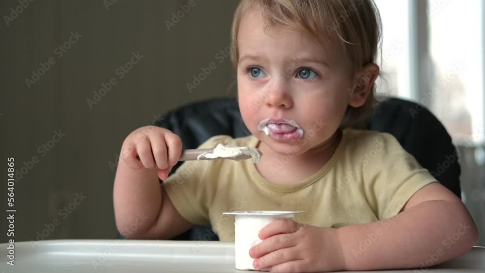 Toddler Sitting in Highchair Eating Greek Yogurt. Funny Cute Baby Eats in the Kitchen. Little Girl Learning to Eat. Child Feeding Himself by Silicone Spoon at Home. Breakfast with Dairy Products. 4K Toddler Sitting in Highchair Eating Greek Yogurt. Funny Cute Baby Eats in the Kitchen. Little Girl Learning to Eat. Child Feeding Himself by Silicone Spoon at Home. Breakfast with Dairy Products. 4K