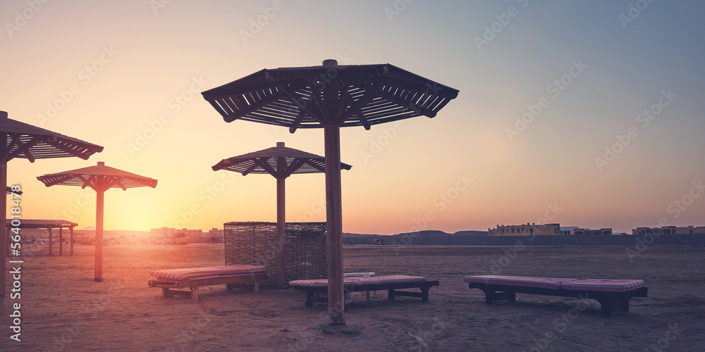 Silhouettes of beach sun umbrellas, beds and windscreen at sunset, color toning applied. Silhouettes of beach sun umbrellas, beds and windscreen at sunset, color toning applied.