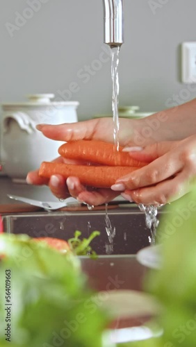 Cropped photo of caucasian overweight woman washing carrot while cooking