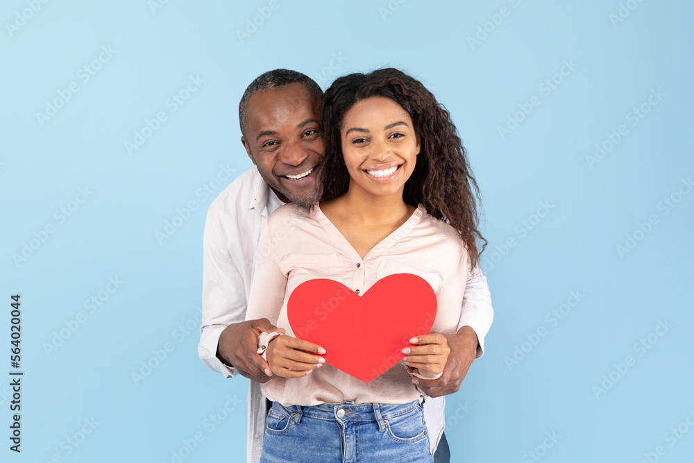 Loving african american couple celebrating their love, black middle aged man and young woman holding big red heart