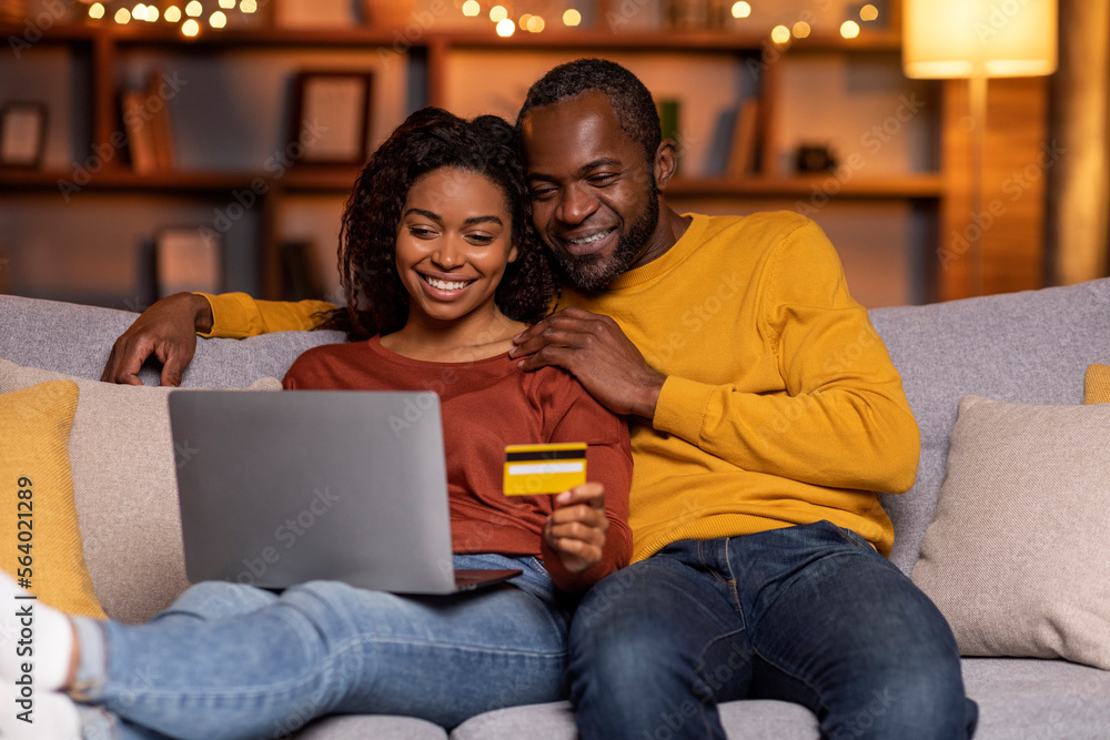 Happy black couple banking from home, using laptop, credit card