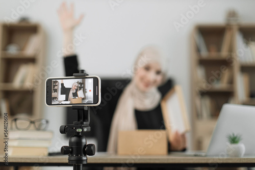Focus on smart phone screen  pleasant arab woman filming video on modern phone camera while opening parcel box. Concept of people  technology and blogging.