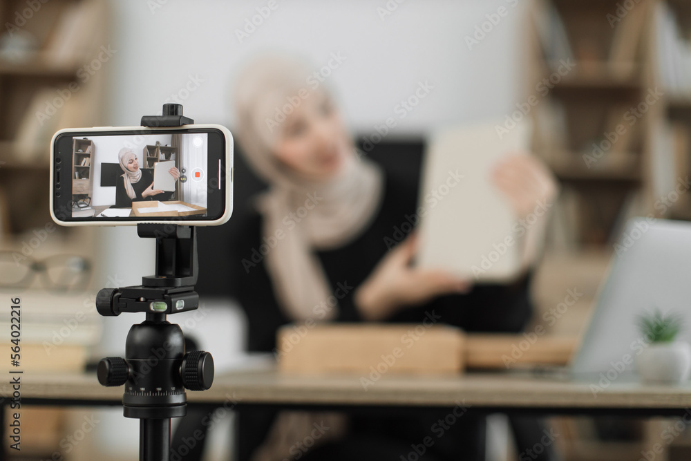 Focus on phone screen , muslim woman recording video on phone camera while unpacking box with new wireless tablet. Female influencer sharing with subscribers her positive feedback about new order. Focus on phone screen , muslim woman recording video on phone camera while unpacking box with new wireless tablet. Female influencer sharing with subscribers her positive feedback about new order.