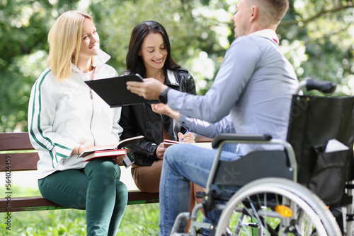 Fotobehang Two female students and one male student study together in park, man is sitting in wheelchair