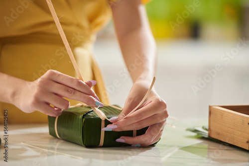 Closeup image of young woman wrapping traditional rice cake in banana leaves