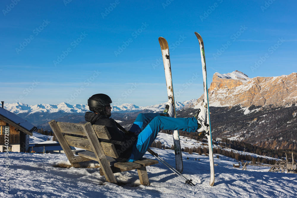 Fototapeta premium Skier resting on a bench overlooking the Italian Dolomites mountains. Ski, winter sport. Narciarz odpoczywa na ławce i podziwia włoskie góry Dolomity. Narty, sporty zimowe. Pralongia.