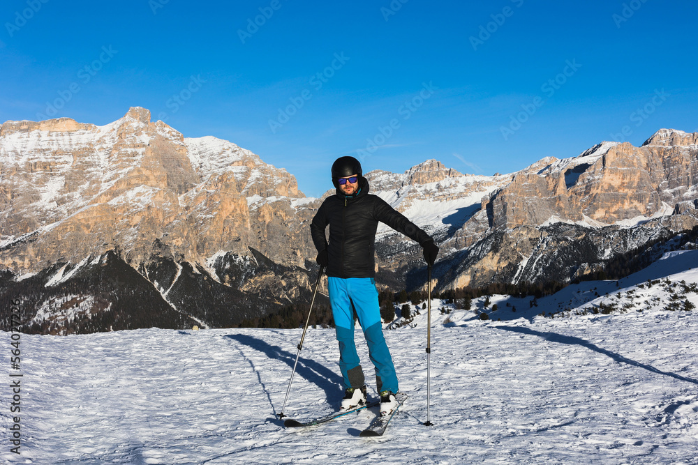 Fototapeta premium A young man, a happy skier, admires the Italian Dolomites mountains. Skiing, winter sports. Młody mężczyzna, szczęśliwy narciarz podziwia włoskie góry Dolomity. Narty, sporty zimowe.