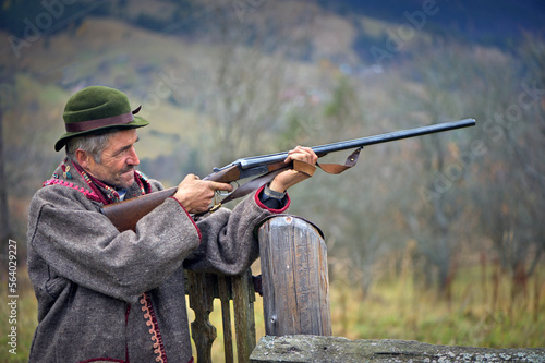 A hunter with a gun in his hands in hunting clothes takes aim and is ready to shoot