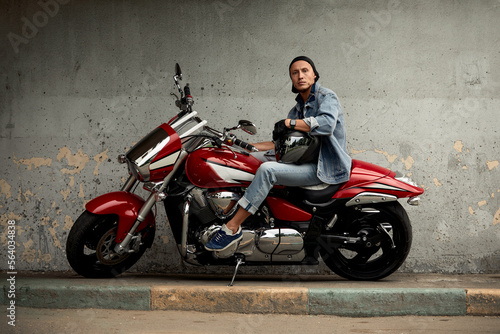 Lifestyle of a motorcyclist  a handsome biker with long hair on a red classic bike in an urban landscape.