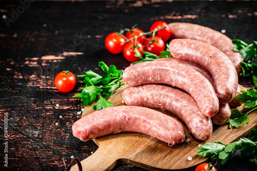 Raw sausages on a wooden cutting board with tomatoes and herbs.