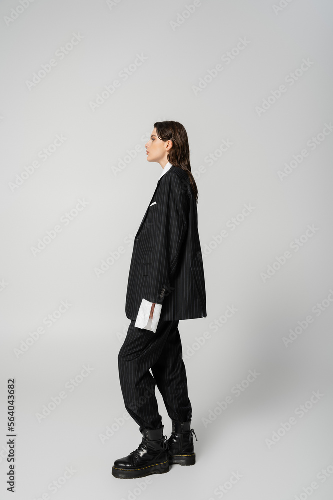 side view of trendy woman posing in black oversize pantsuit and rough boots on grey background. side view of trendy woman posing in black oversize pantsuit and rough boots on grey background.