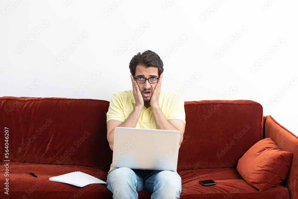 Upset man sitting on the couch and working on laptop at home. Online education and distant work concept Upset man sitting on the couch and working on laptop at home. Online education and distant work concept