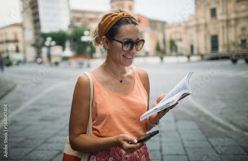 Картината върху платно Cheerful woman wander with travel guidebook and smart phone