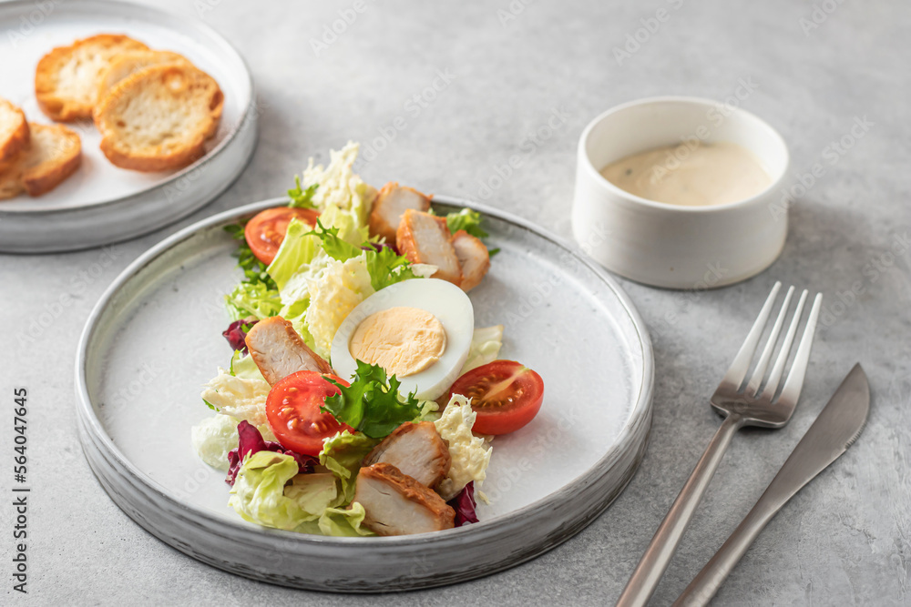 Caesar salad in modern linear feed with chicken, egg, tomatoes, lettuce and parmesan chips with cutlery on gray table, menu Caesar salad in modern linear feed with chicken, egg, tomatoes, lettuce and parmesan chips with cutlery on gray table, menu