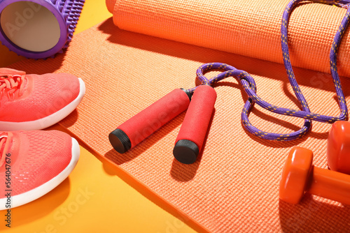 Skipping rope with fitness mat on color background, closeup