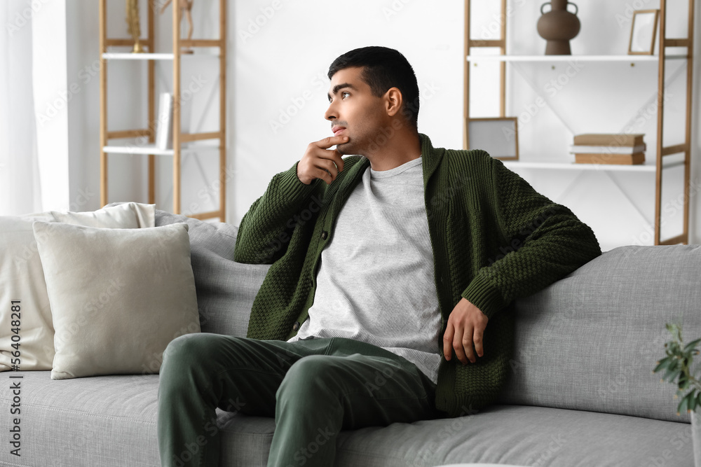Fototapeta premium Thoughtful young man sitting on sofa at home