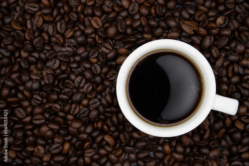 A white cup with coffee on a background of coffee beans. top view.