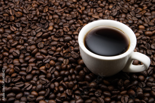 A white cup with coffee on a background of coffee beans. top view.