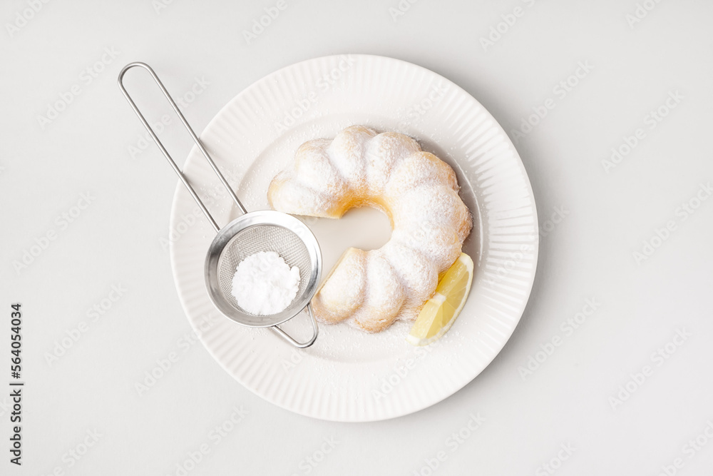 Plate with delicious cake, sieve of powdered sugar and lemon slice on white background Plate with delicious cake, sieve of powdered sugar and lemon slice on white background
