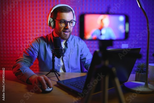 vlogger using smartphone to film podcast in studio. blogger with mobile phone, microphone and headphones filming video for social media broadcasting career.