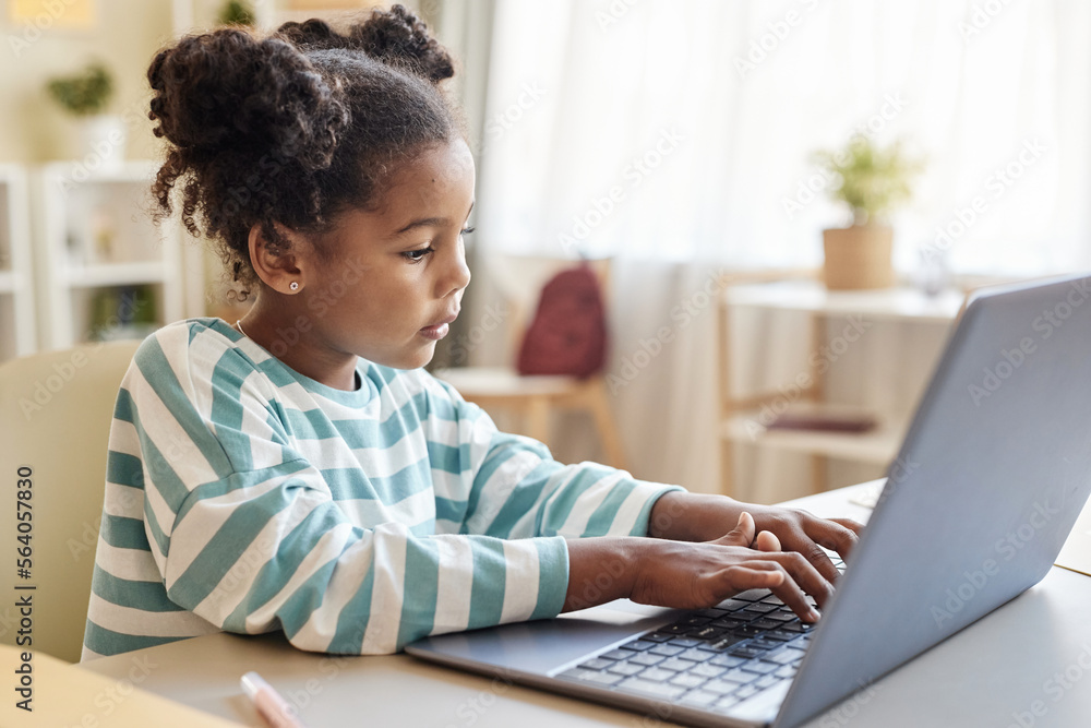 Side view cute black little girl using laptop studying online at home Side view cute black little girl using laptop studying online at home