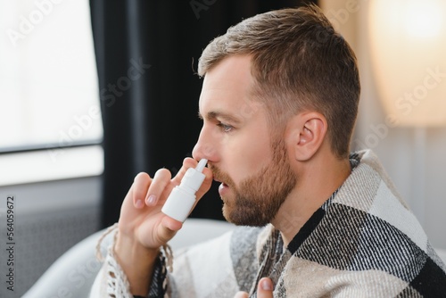 Sick man with nasal spray and paper tissue at home
