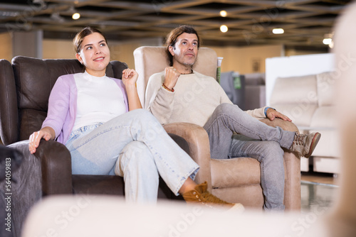 Joyful man and woman in furniture store in process of selecting new chair for home