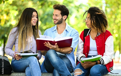 Three multiethnic students studying together sitting on a bench outdoor
