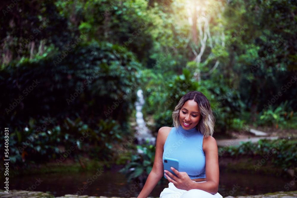 young brazilian woman holding the cell phone looking at the screen smiling outdoors in a park young brazilian woman holding the cell phone looking at the screen smiling outdoors in a park