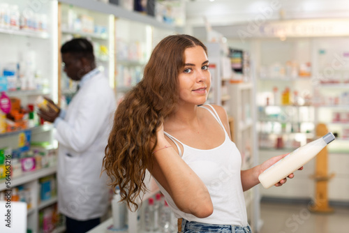 Brown-haired young lady choosing haircare products in drugstore