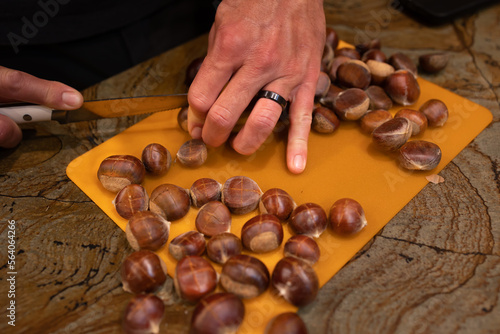 A horizontal photo a young caucasian man preparing brown Chestnuts for roasting by cutting X's in the nuts with a long knife.  photo