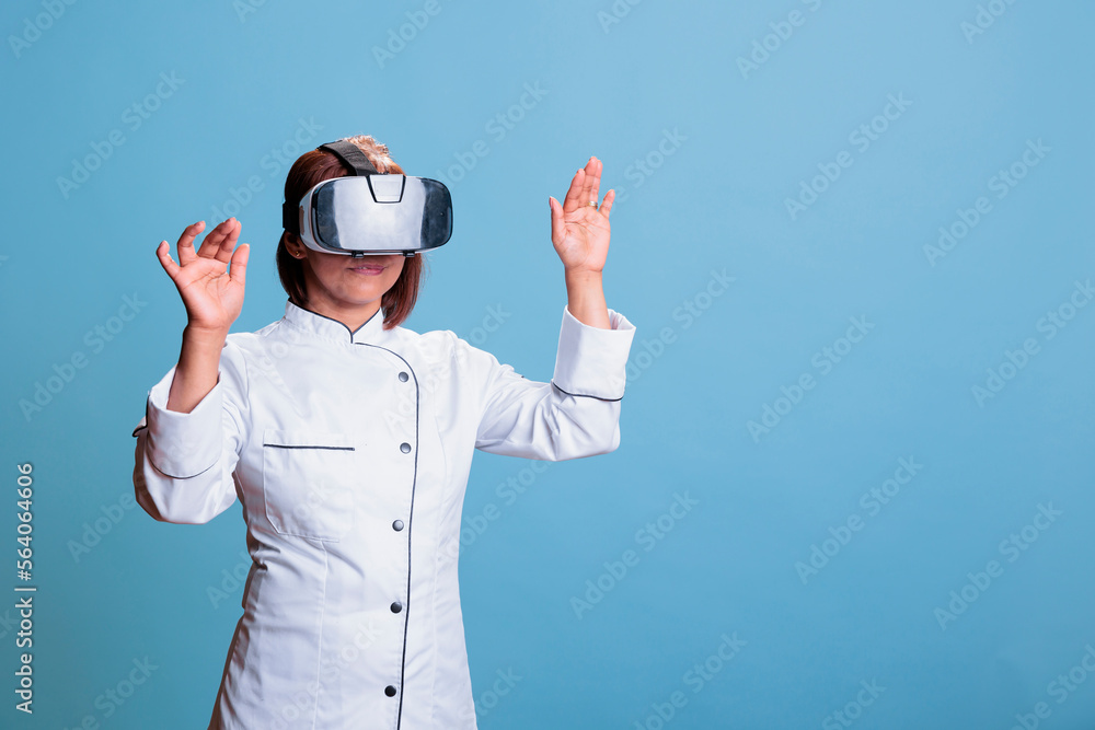 Friendly cook worker using virtual reality goggles while cooking healthy meal in studio with blue background. Asian chef preparing culinary recipe for restaurant. Food industry concept Friendly cook worker using virtual reality goggles while cooking healthy meal in studio with blue background. Asian chef preparing culinary recipe for restaurant. Food industry concept