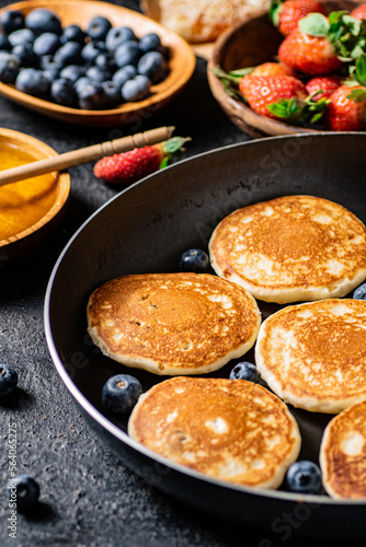 Pancakes in a frying pan with fresh berries and honey. 