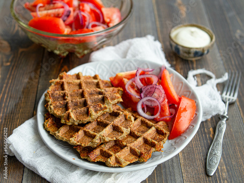 Delicious eggplant wafflese inwhite ceramic plate with tomato and onion salad and sauce ion wood background. Healthy vegeterian food. Close up, copy space.
