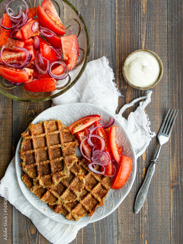 Delicious eggplant wafflese inwhite ceramic plate with tomato and onion salad and sauce ion wood background. Healthy vegeterian food. Close up, copy space.