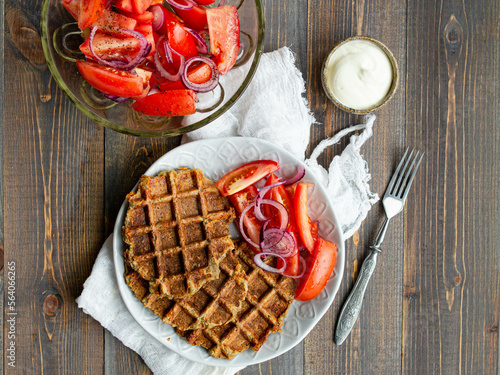 Delicious eggplant wafflese inwhite ceramic plate with tomato and onion salad and sauce ion wood background. Healthy vegeterian food. Close up, copy space.