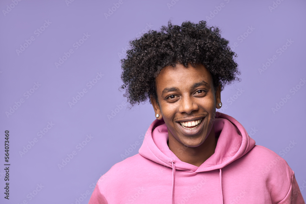 Young happy hipster African American teen guy wearing pink hoodie isolated on purple background. Smiling cool ethnic generation z teenager student model standing looking at camera posing for portrait. - obrazy, fototapety, plakaty 