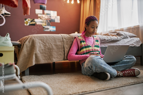 Black teenage girl using laptop indoors sitting on floor