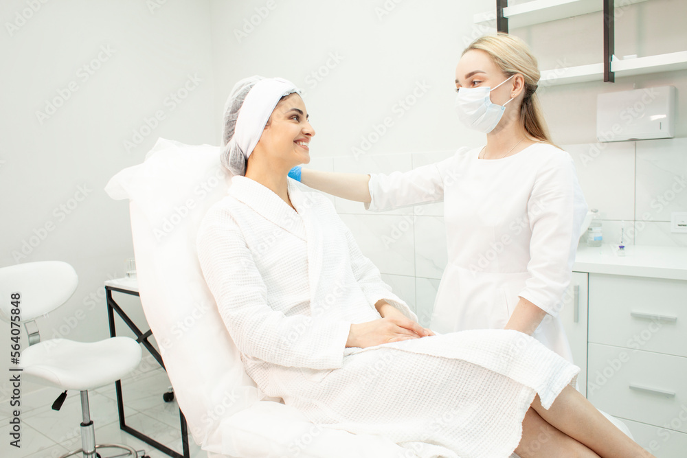 Fototapeta premium female patient in a white coat sits on a couch in a cosmetology clinic at the appointment of cosmetologist