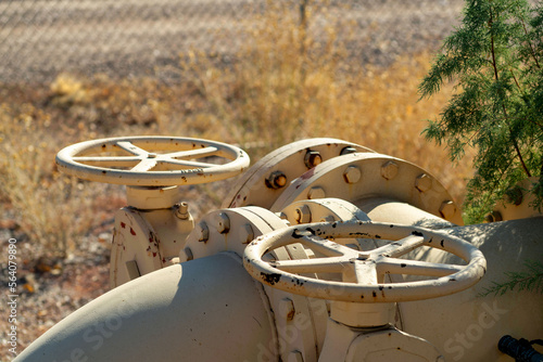 Hand wheels on valves and pipes with beige color and natural tree and grass background in late afternoon sun